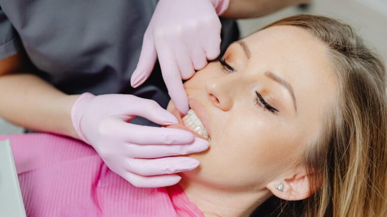 A dentist wearing gloves examines a patient's teeth in a close-up view during a dental check-up.
