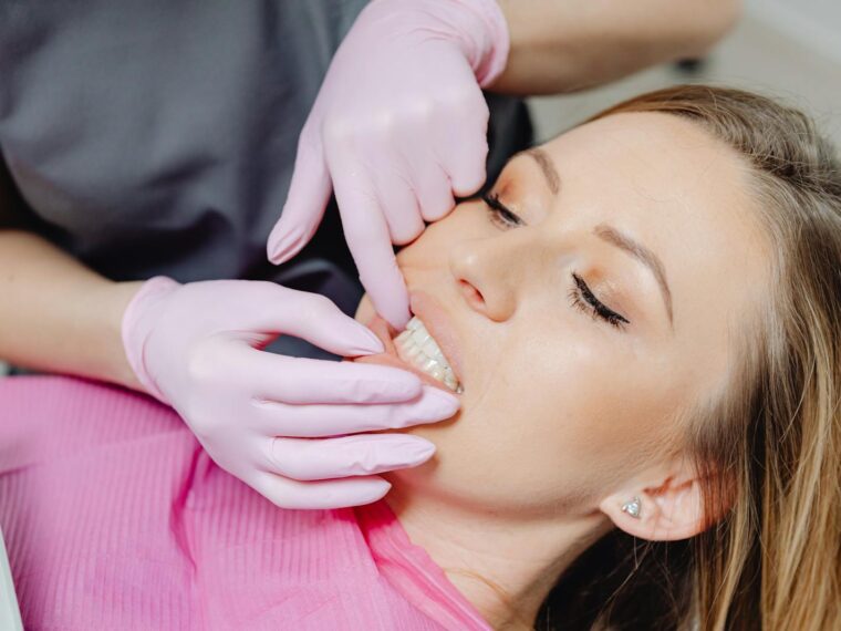 A dentist wearing gloves examines a patient's teeth in a close-up view during a dental check-up.