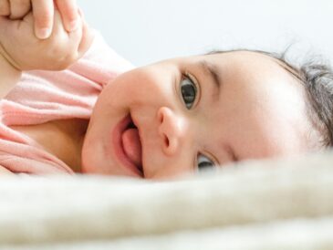 baby in pink shirt lying on white textile