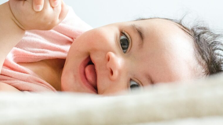 baby in pink shirt lying on white textile